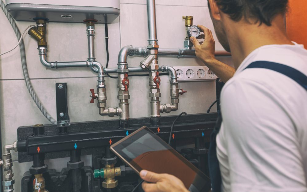 A Man Is Working on A Pipe System While Holding a Tablet — Sydney Underfloor Heating in Woonona, NSW