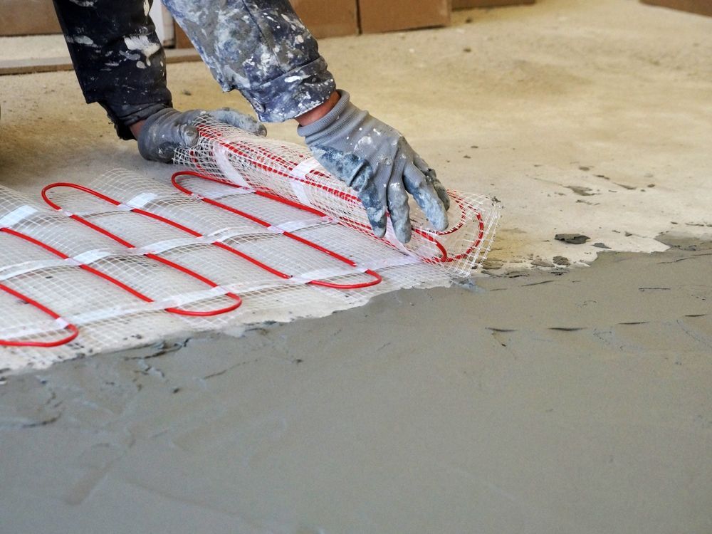A Person Is Installing a Heat Mat on A Concrete Floor — Sydney Underfloor Heating in Woonona, NSW