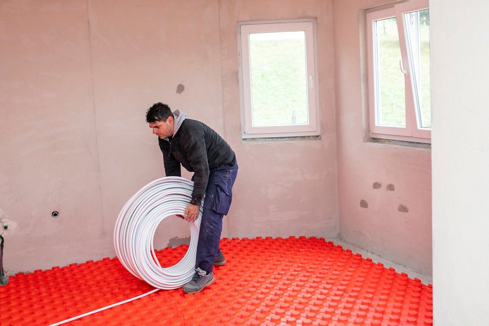 A Man Is Holding a Roll of Pipe in A Room — Sydney Underfloor Heating in Sydney, NSW
