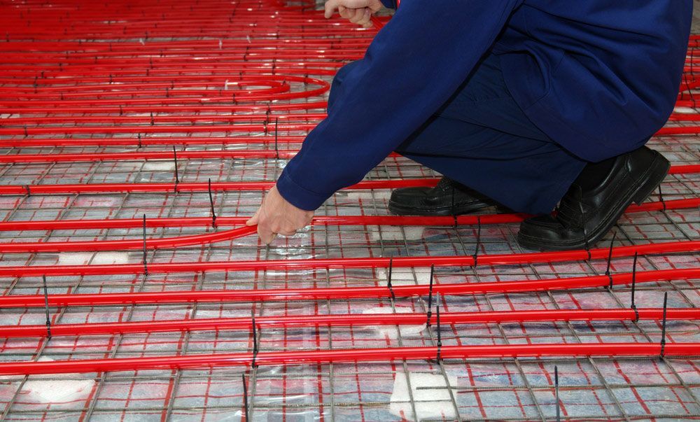 Worker Is Installing A Red Pipe For The Warm Floor Mounting The System Underfloor Heating — Sydney Underfloor Heating in Sydney, NSW