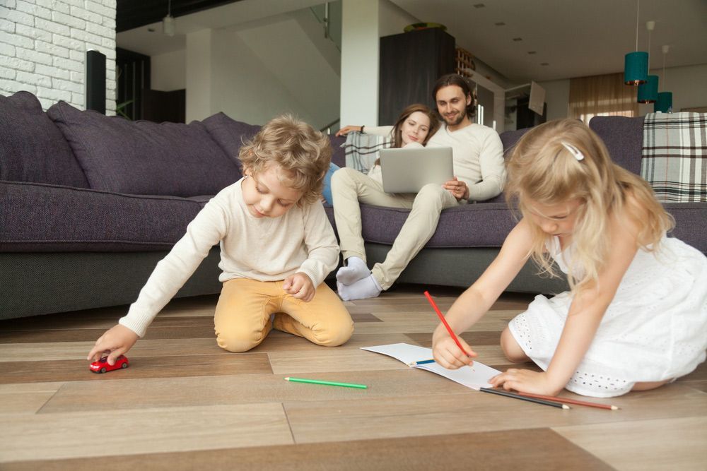 Kids Siblings Playing On Floor While Parents Using Laptop At Home — Sydney Underfloor Heating in Woonona, NSW