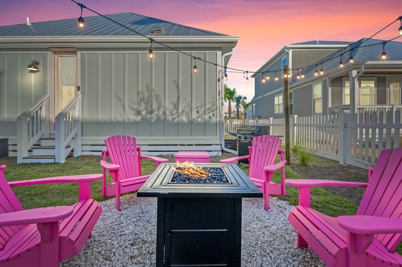 Backyard fire pit with pink Adirondack chairs under string lights at sunset.