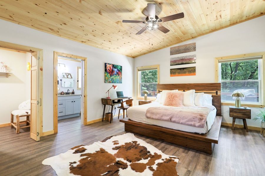 Bedroom with wood ceiling, brown bed, pink accents, desk, and bathroom entry.