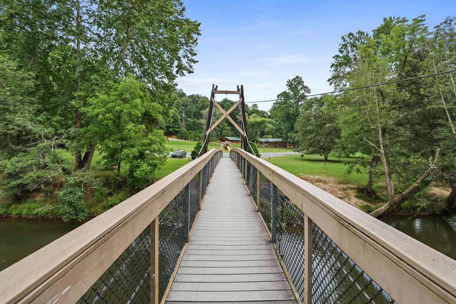 Wooden footbridge spanning a river, with green trees and a grassy bank.