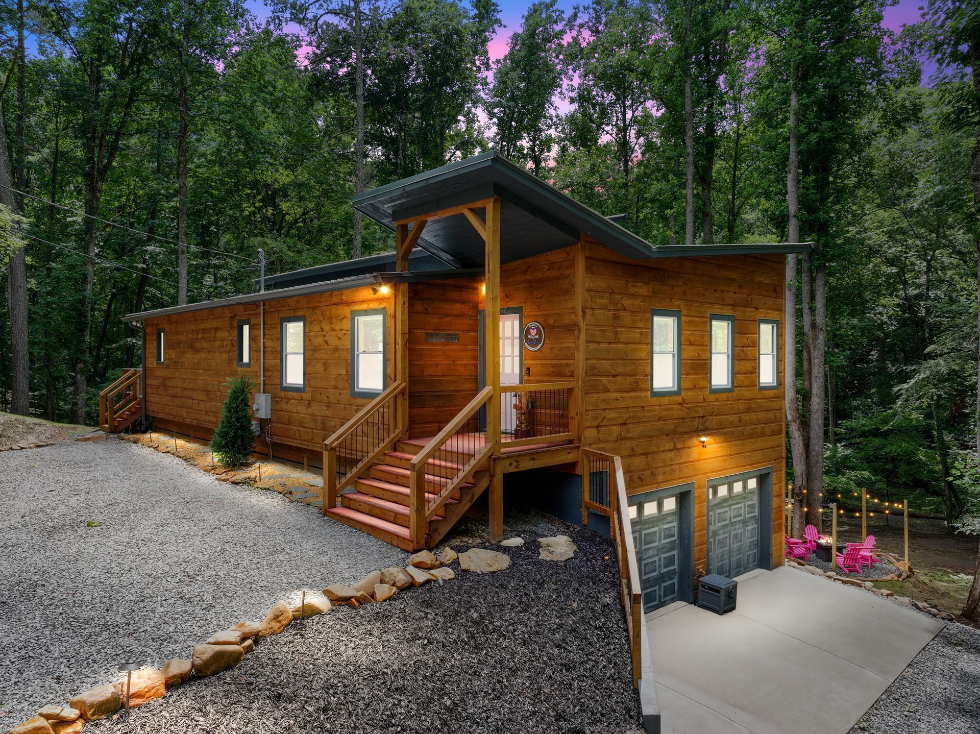 Wooden cabin with steps, garage, and gravel driveway, surrounded by trees.