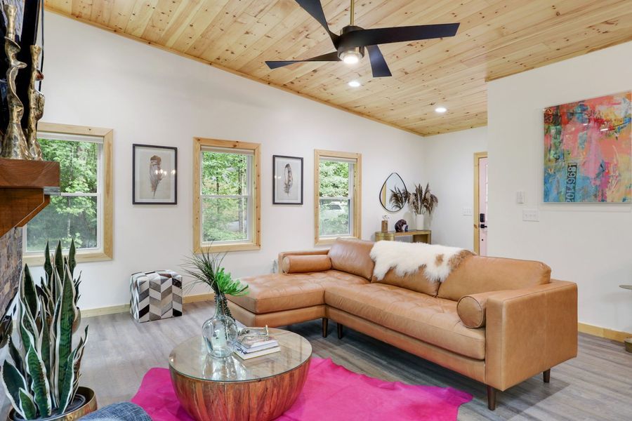 Living room with wood ceiling, brown sectional, pink rug, and large colorful artwork.