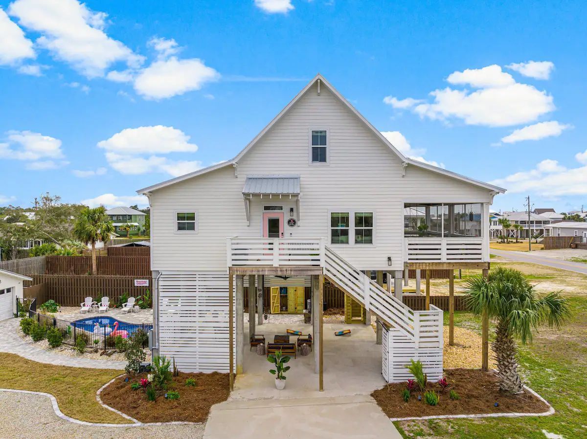 White beach house with raised foundation, outdoor dining, and pool.