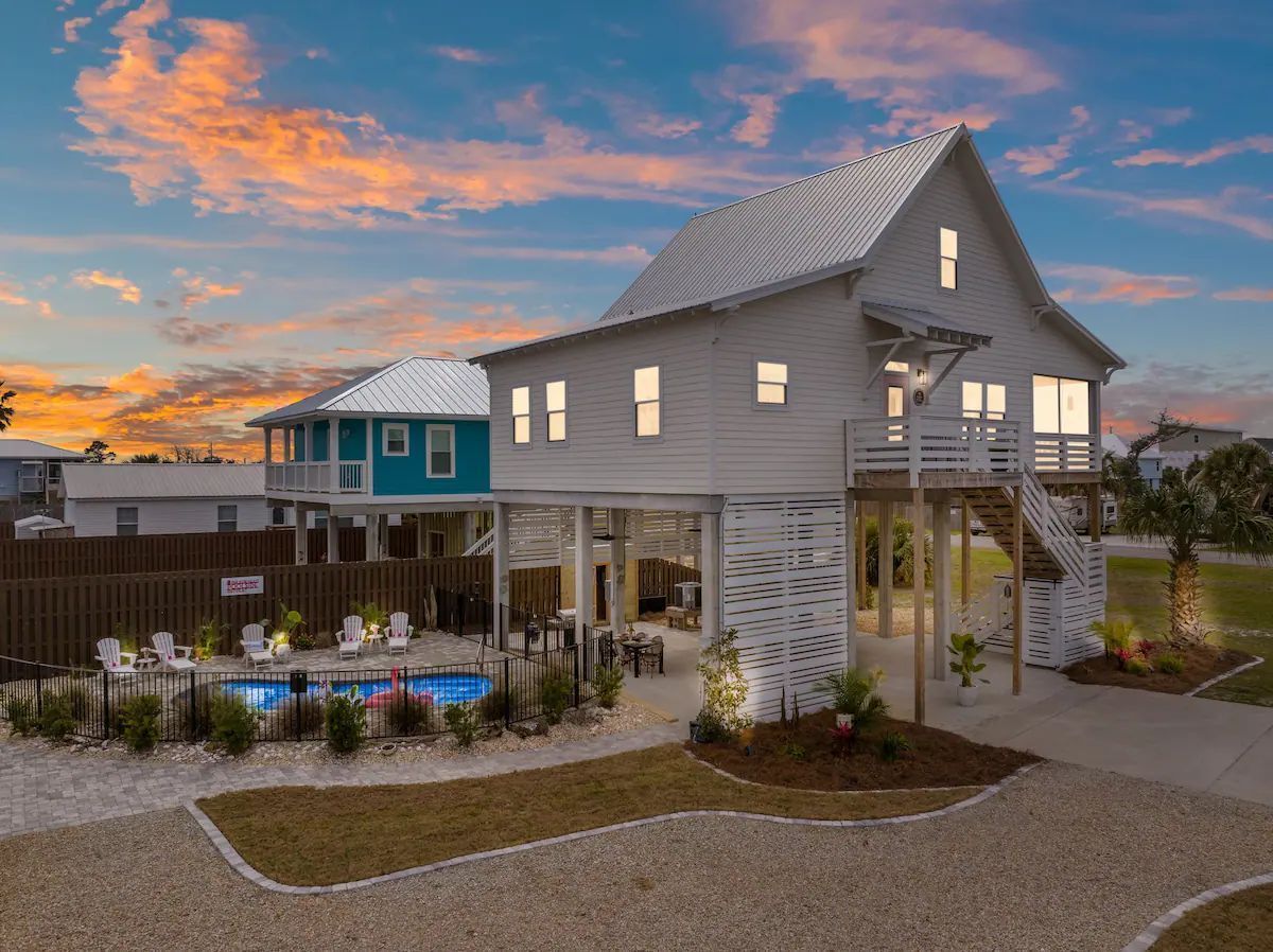White beach house on stilts with pool at sunset.