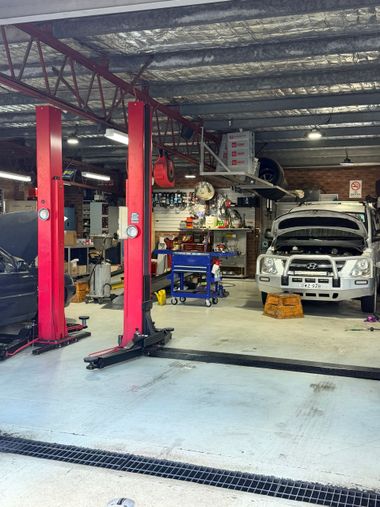 Auto repair shop with red lifts, a white SUV, and tools under a metal roof