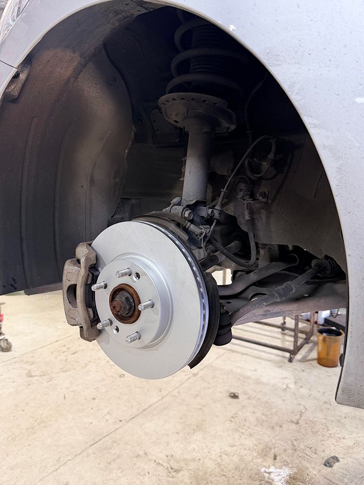 Close-up of a car’s front wheel hub, brake rotor, and suspension inside the wheel well.