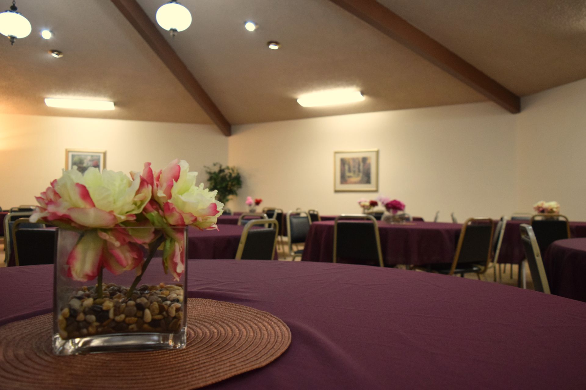 A vase of flowers sits on a table in a room with tables and chairs.