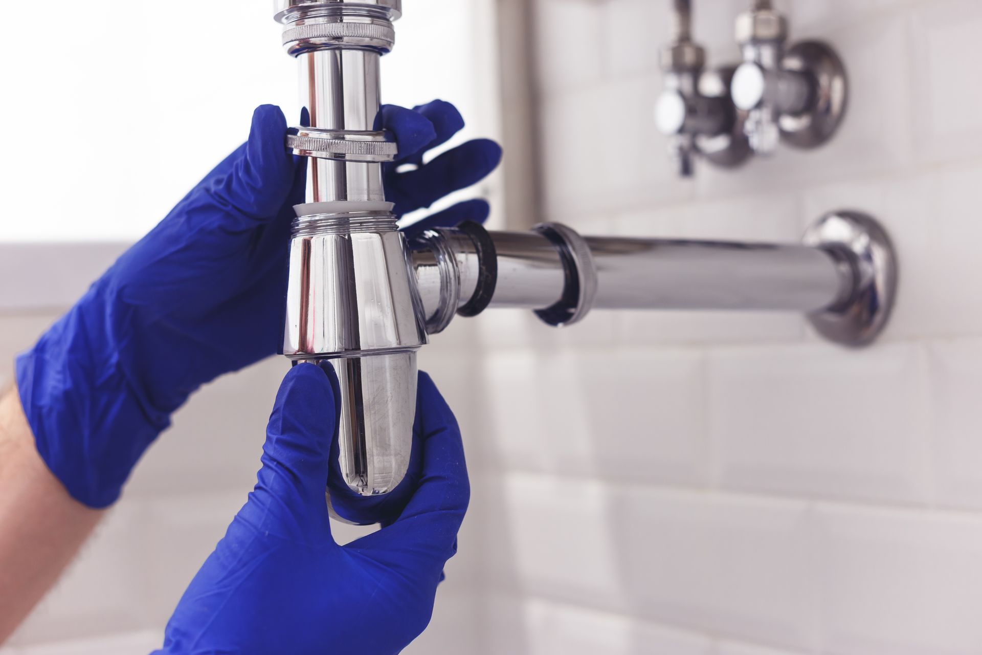 Gloved hands installing a chrome sink drain pipe under a bathroom sink Gloved hands installing a chrome sink drain pipe under a bathroom sink