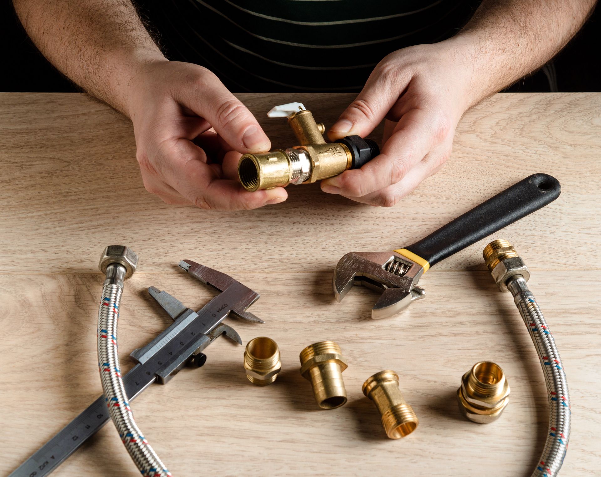 Hands assembling brass plumbing fittings with a wrench and caliper on a wooden workbench Hands assembling brass plumbing fittings with a wrench and caliper on a wooden workbench
