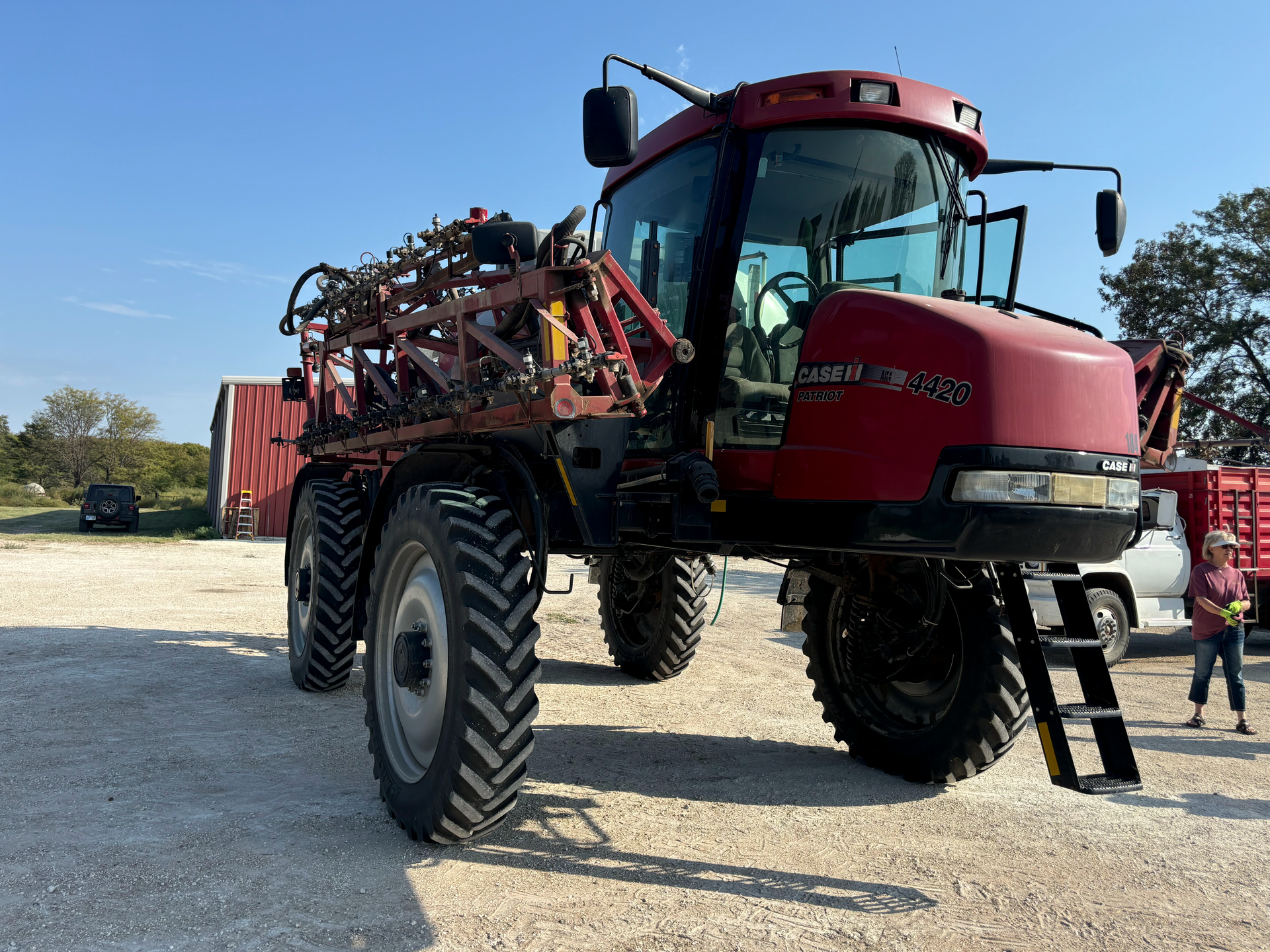 A red tractor with a ladder attached to it is parked in a dirt lot.