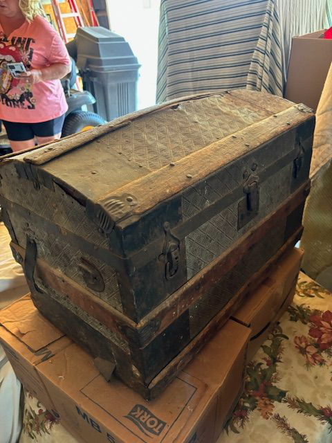 An old wooden trunk is sitting on top of a pile of cardboard boxes.