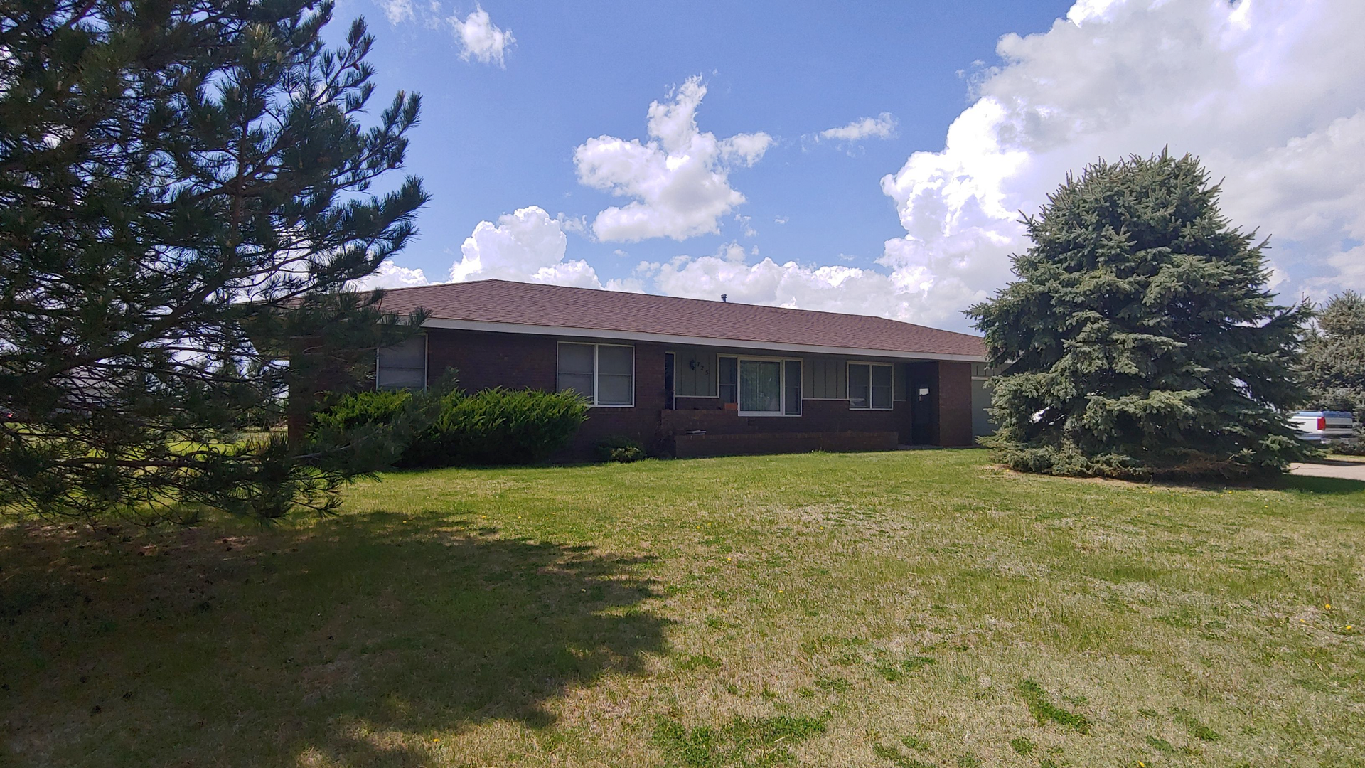 A brick house with a red roof and a large lawn in front of it.