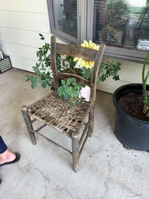 A wooden chair is sitting on a porch next to a potted plant.