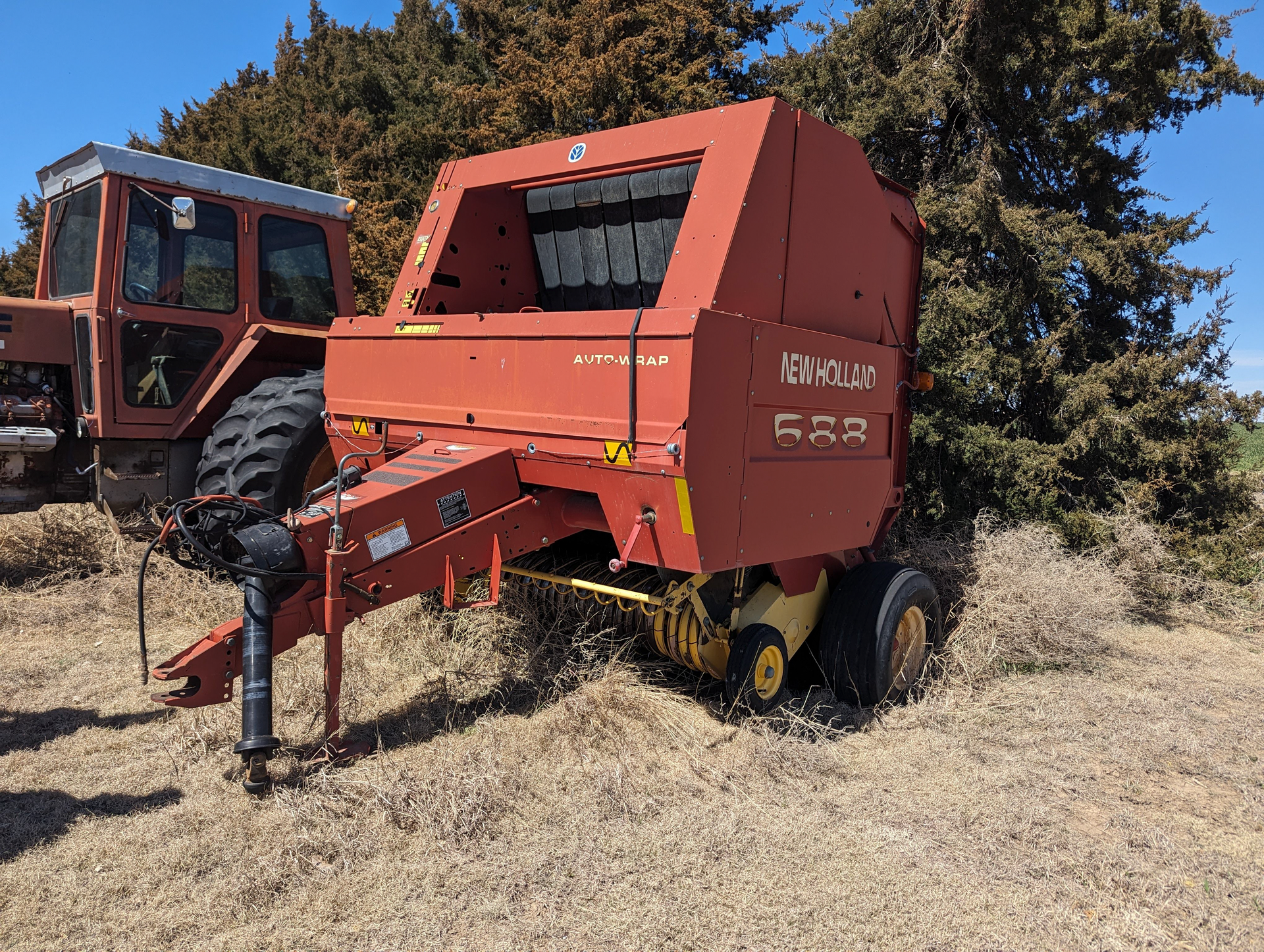 A red hay baler is parked in a field next to a tractor.
