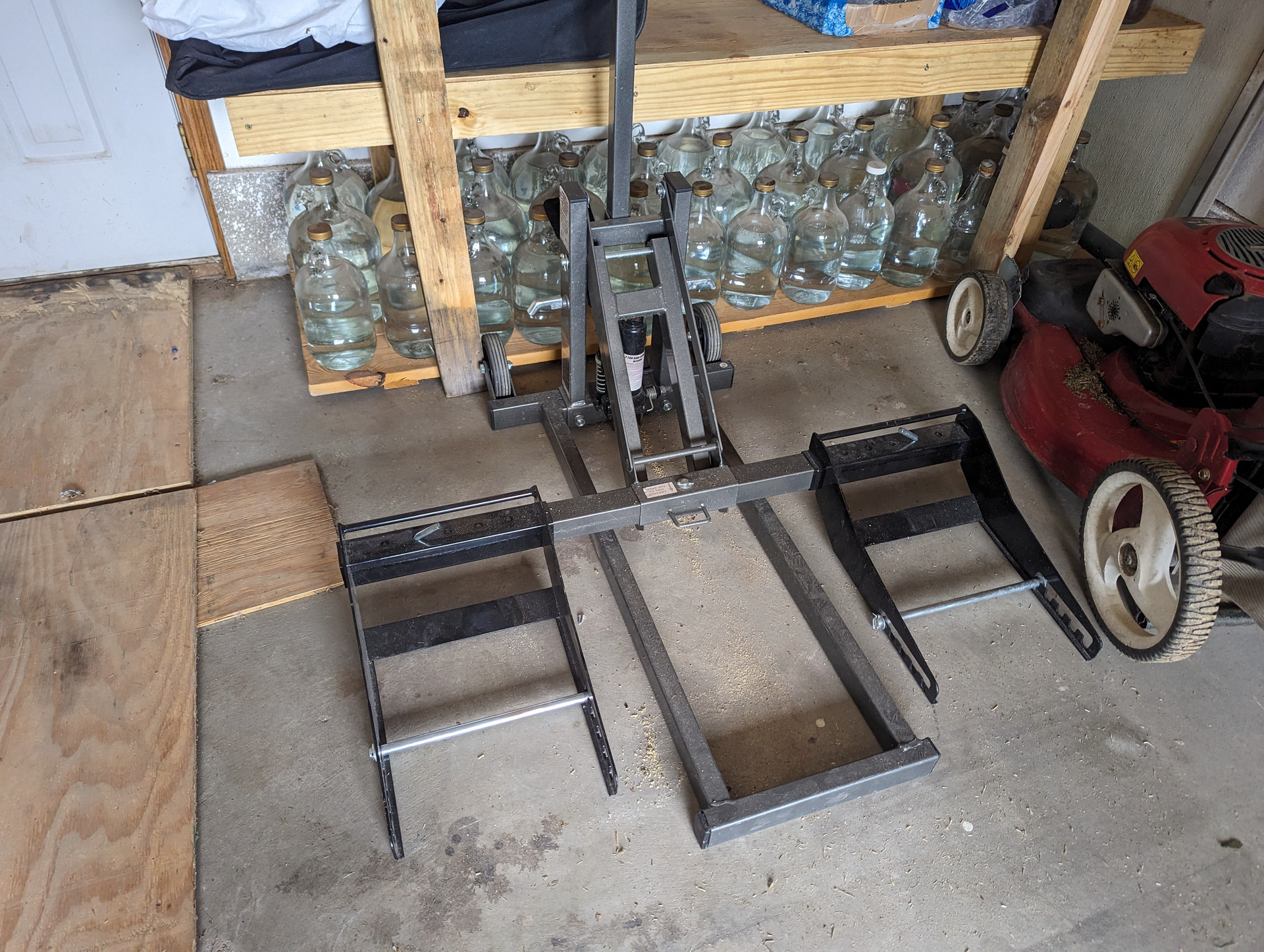 A lawn mower is parked next to a motorcycle lift in a garage.