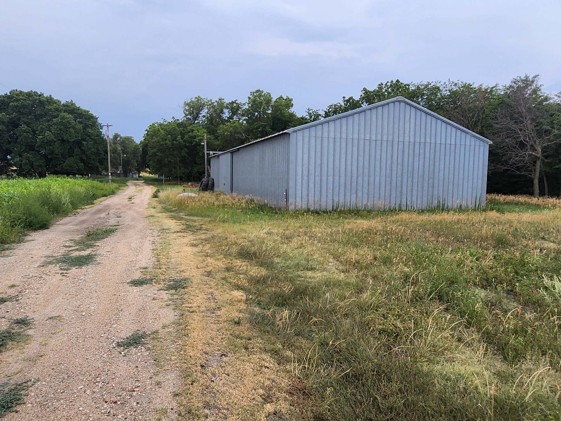 A large metal building is sitting in the middle of a field next to a dirt road.