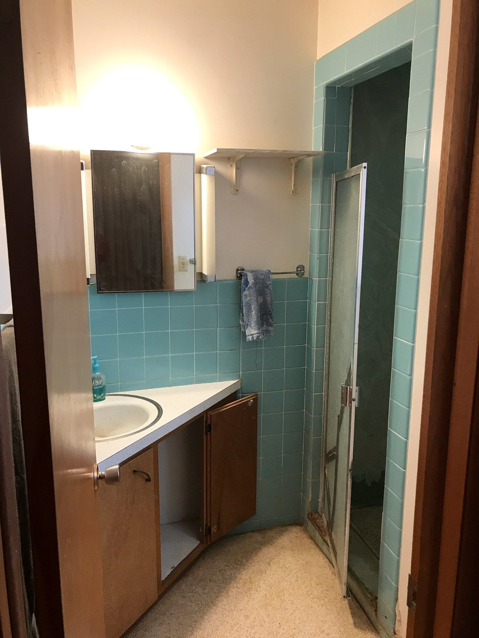 A bathroom with blue tiles , a sink , and a shower.