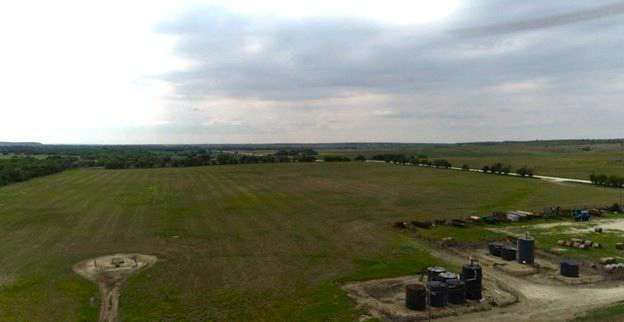 An aerial view of a large grassy field with a cloudy sky in the background.