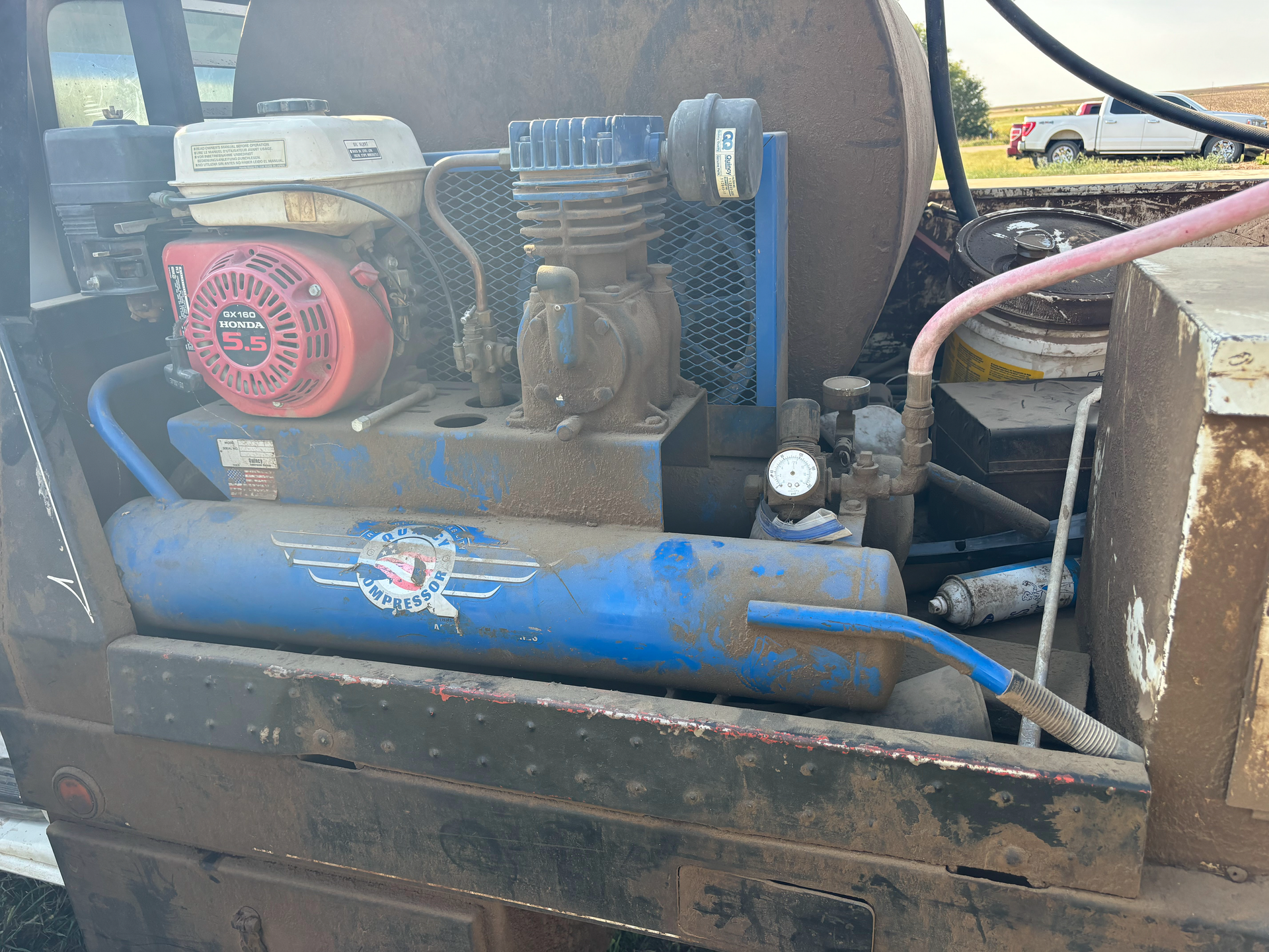A dirty air compressor is sitting on top of a truck.