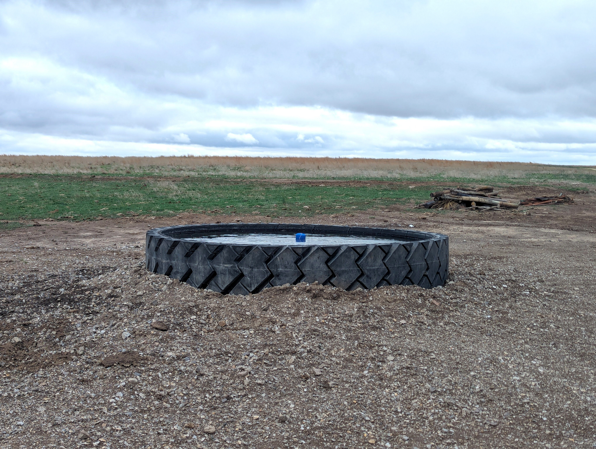 A large tire is sitting in the middle of a gravel field.