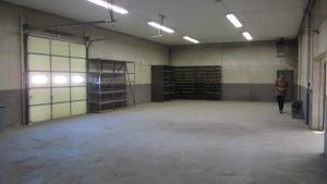 A large empty warehouse with a garage door and shelves.