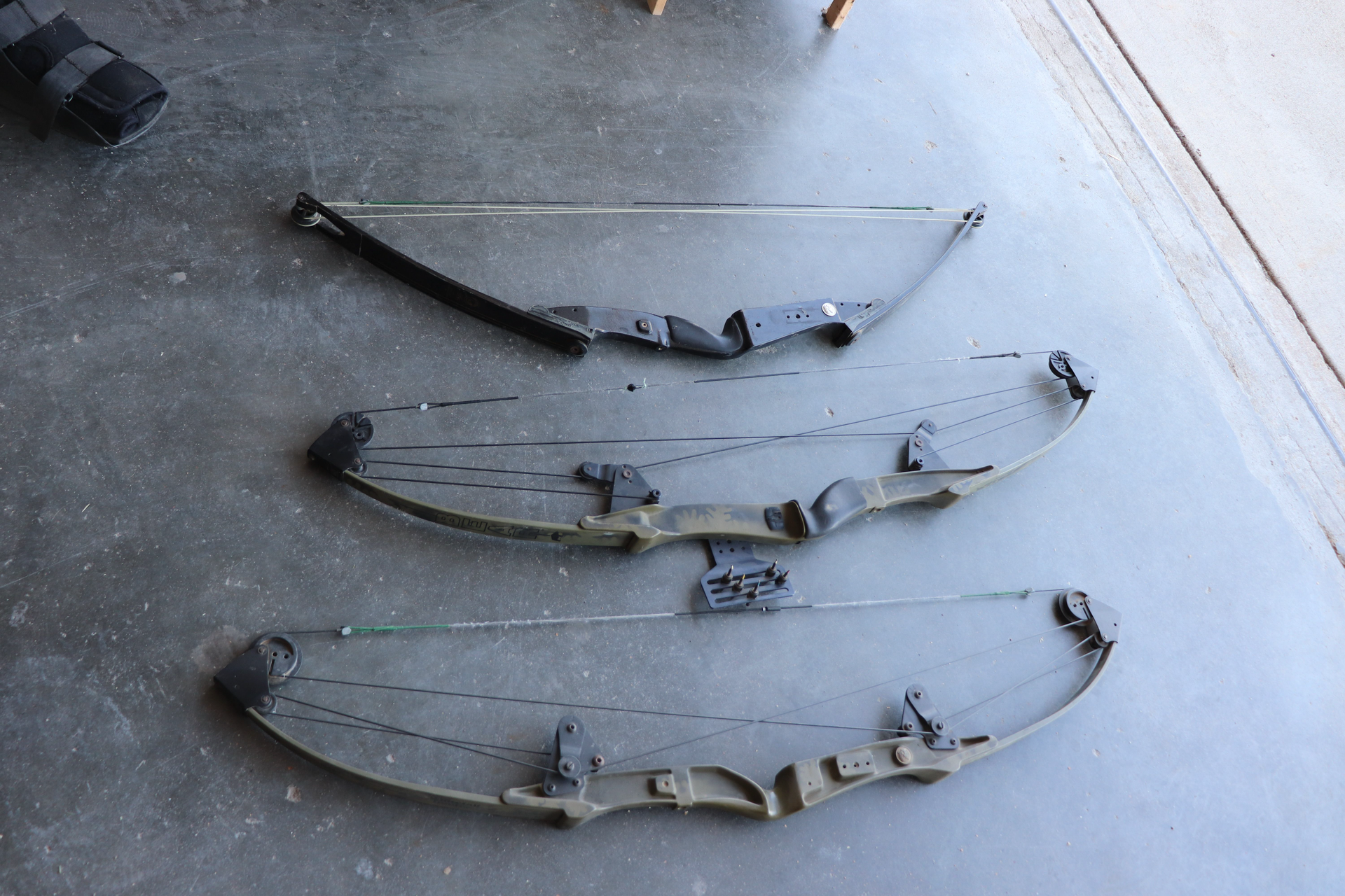 Three archery bows are lined up on a concrete surface