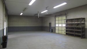 A large empty warehouse with a garage door and shelves.