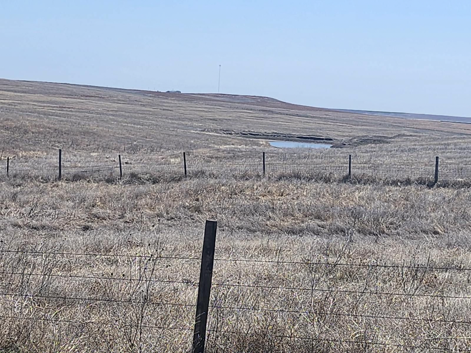 A barbed wire fence surrounds a dry grassy field