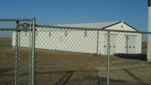 A chain link fence surrounds a white building in a field.