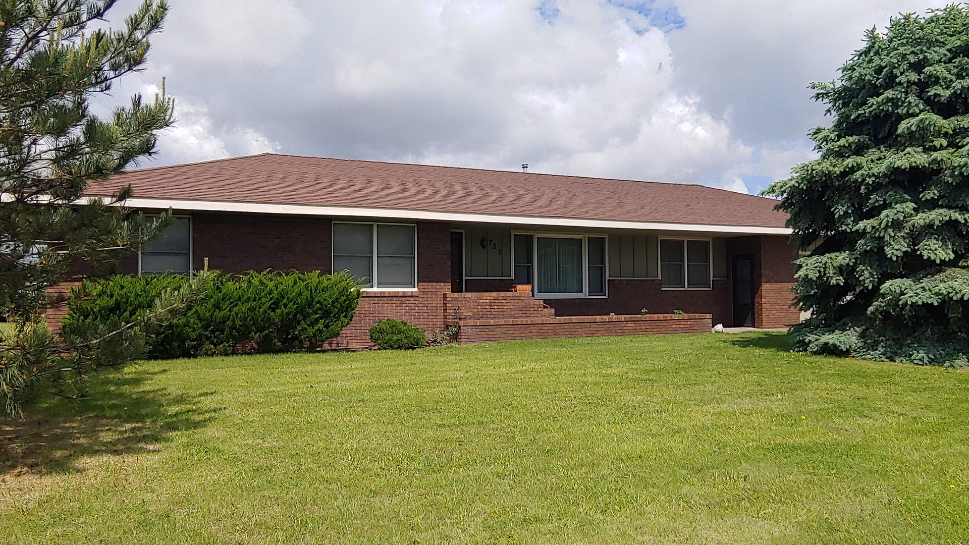 A brick house with a red roof and a large lawn in front of it.
