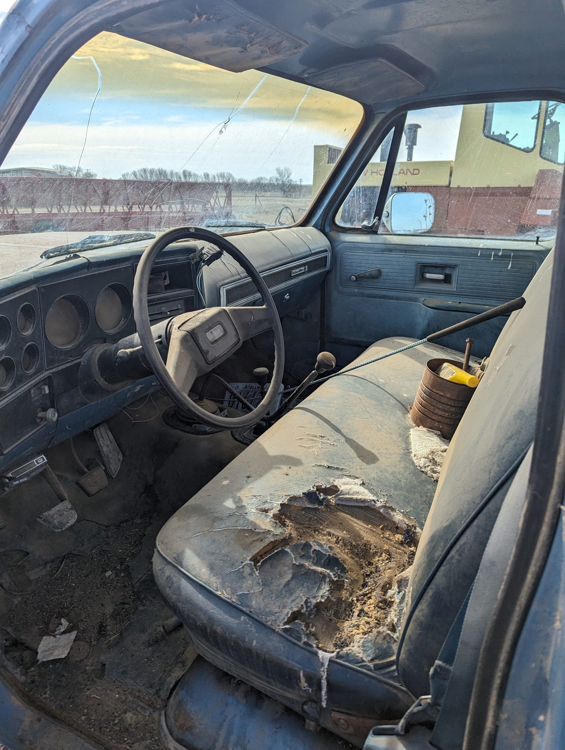 The interior of an old truck with a broken seat and steering wheel.