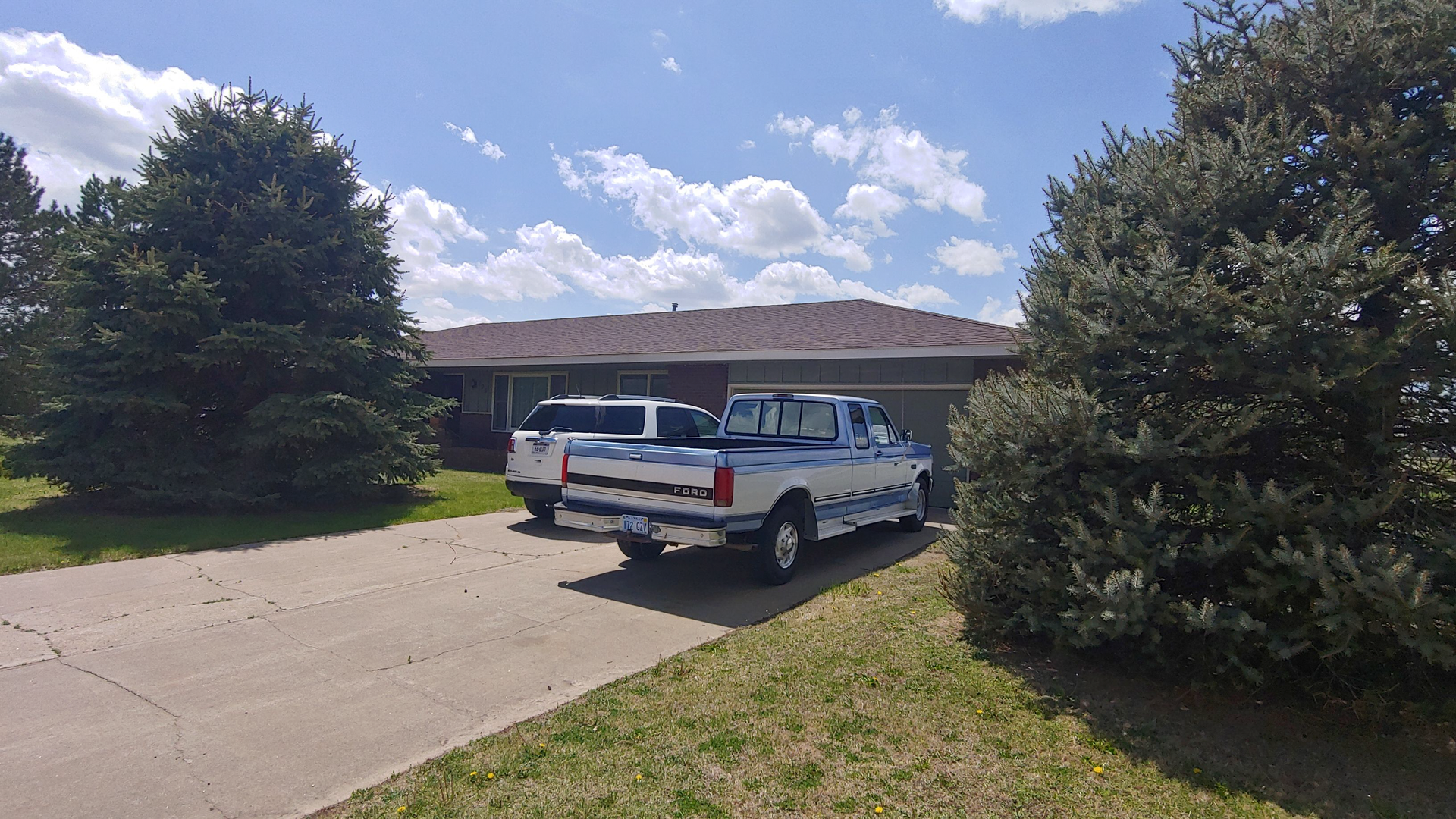 Two white trucks are parked in front of a house.