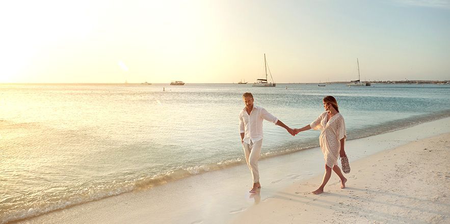Un hombre y una mujer caminan por la playa tomados de la mano.