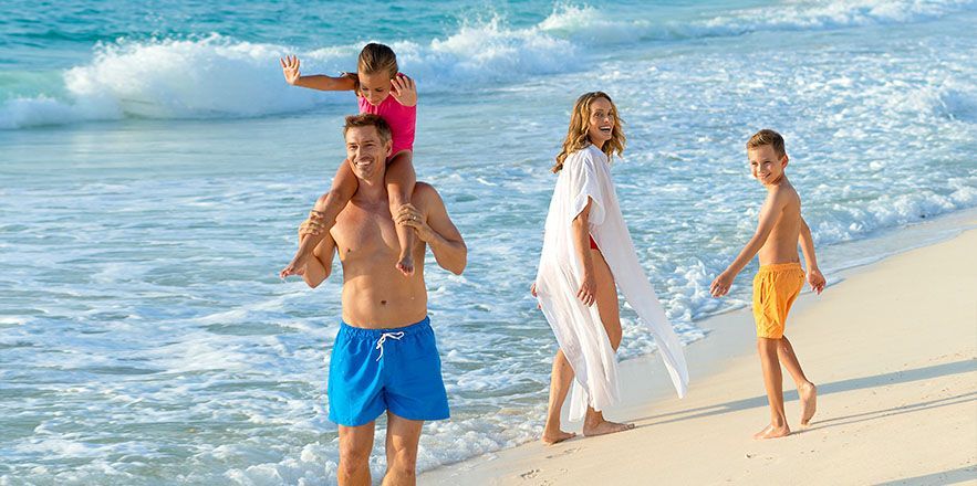 Una familia camina por la playa con un hombre que lleva a un niño sobre sus hombros.