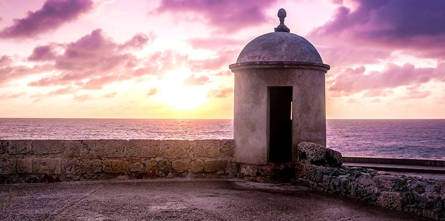Un pequeño edificio con una puerta se encuentra junto al océano al atardecer.