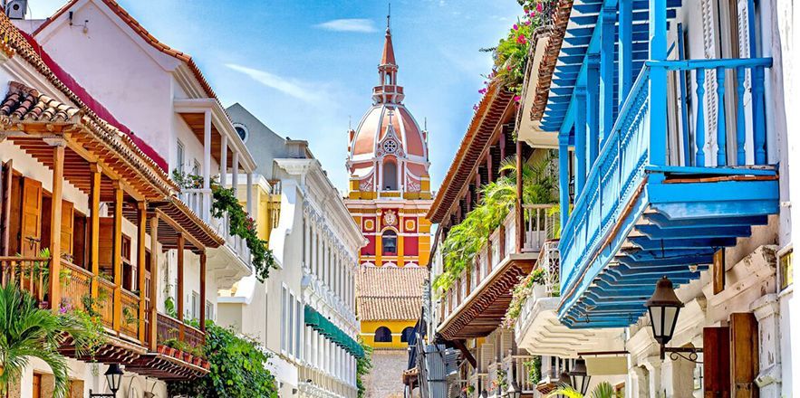 Una calle estrecha bordeada de edificios y balcones con una torre de reloj al fondo.