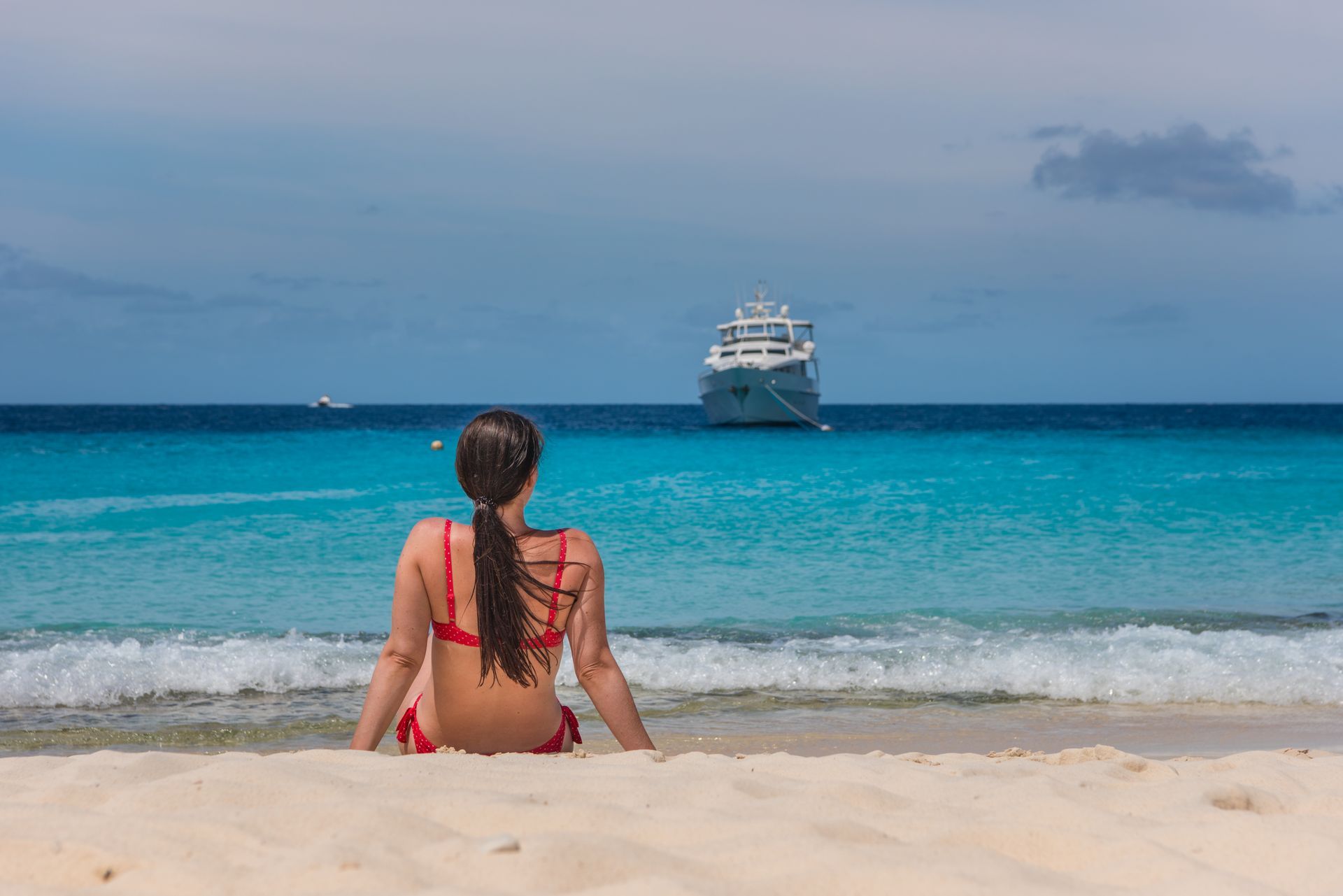 Una mujer está sentada en la playa mirando un crucero en el océano.