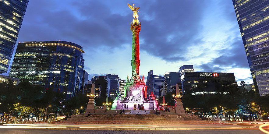 Una gran estatua está iluminada con los colores de la bandera mexicana.