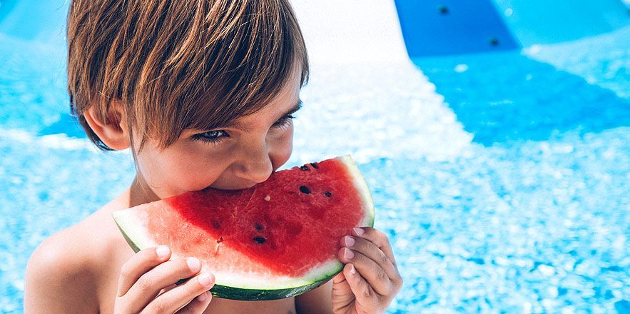 Un niño está comiendo una rodaja de sandía en una piscina.