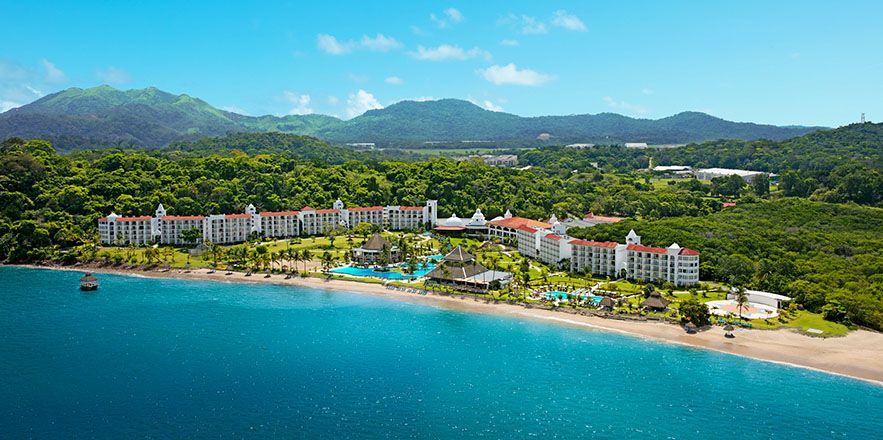 Una vista aérea de un resort en una isla tropical con montañas al fondo.