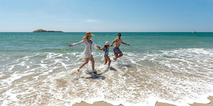 Una familia corre hacia el océano en una playa.