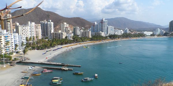 Una playa con una ciudad al fondo y barcos en el agua.