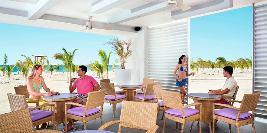 Un grupo de personas están sentadas en mesas en una playa.