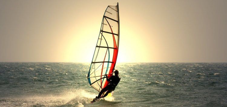 Un hombre practica windsurf en el océano al atardecer.