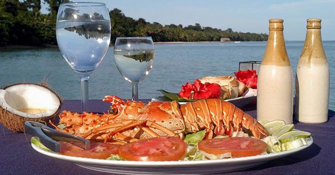 Un plato de comida con una langosta está sobre una mesa junto al océano.