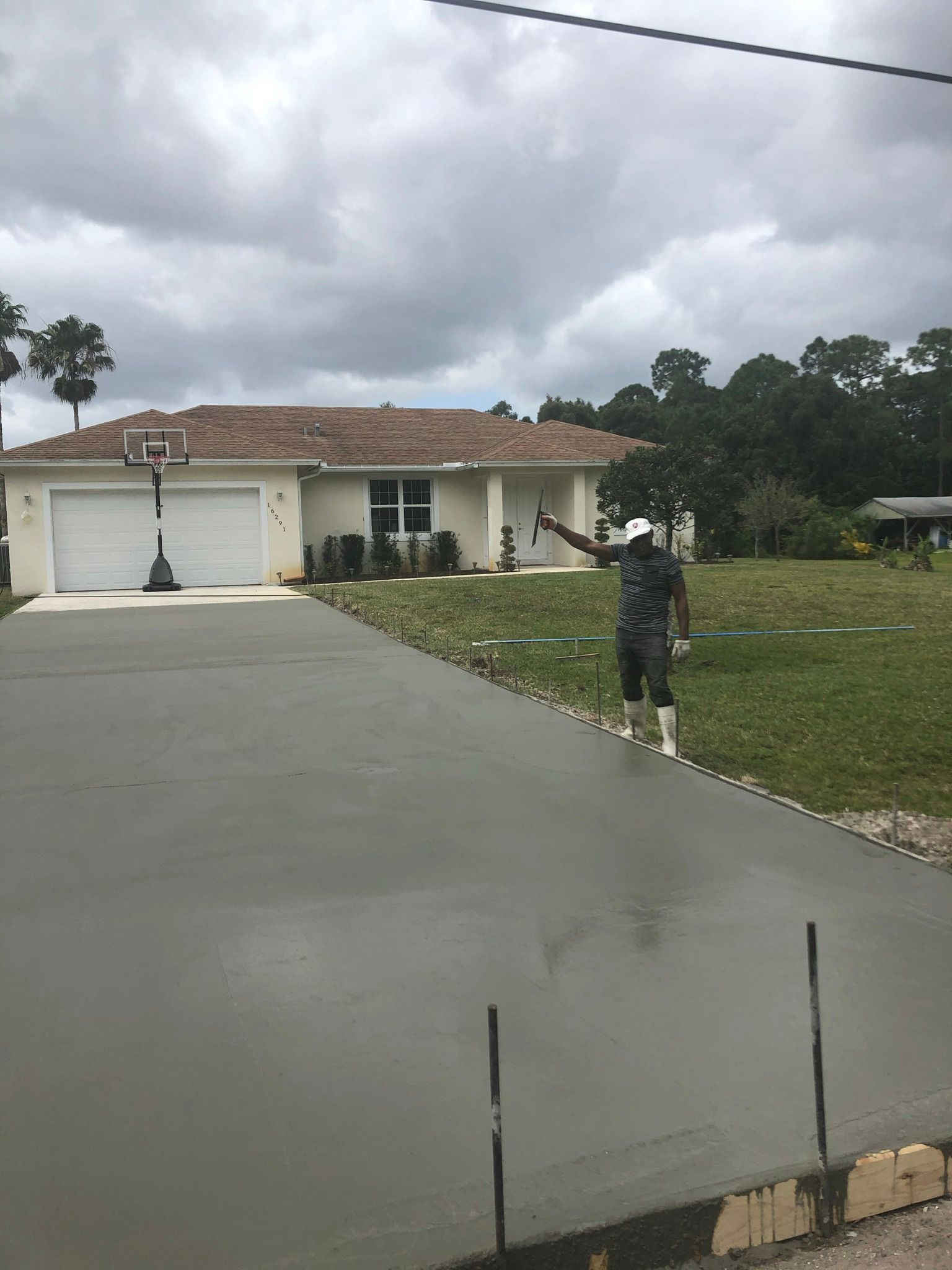 A man is pouring concrete into a driveway in front of a house.